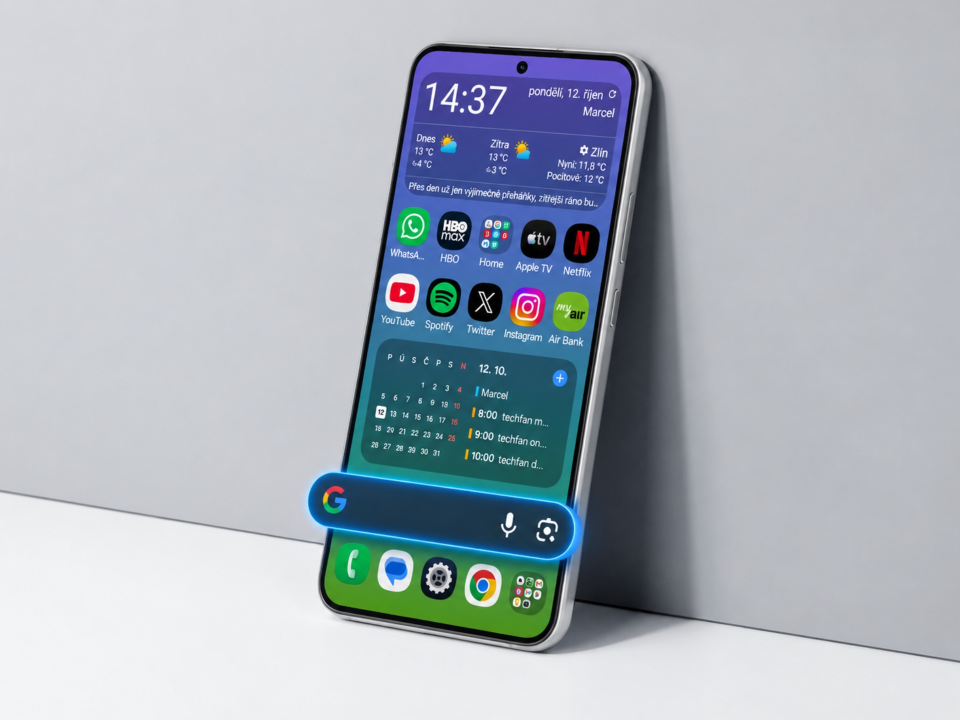 Mobil Samsung Galaxy S26 s domovskou obrazovkou, ikonami aplikací a modrým vyhledávacím panelem Google.
