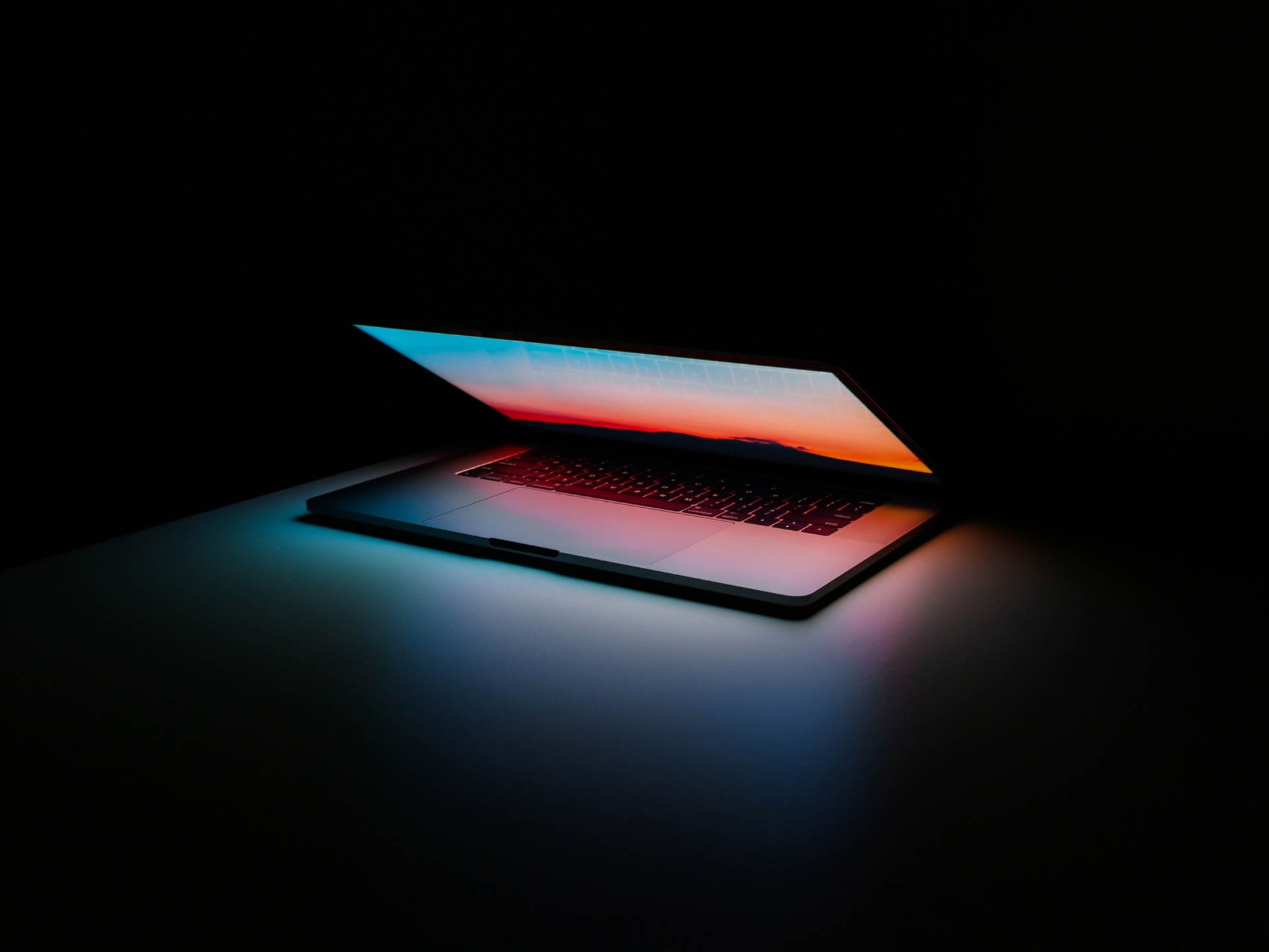 Otevřený notebook googlebook s podsvícenou klávesnicí, barevná světla modro-červená na tmavém pozadí.