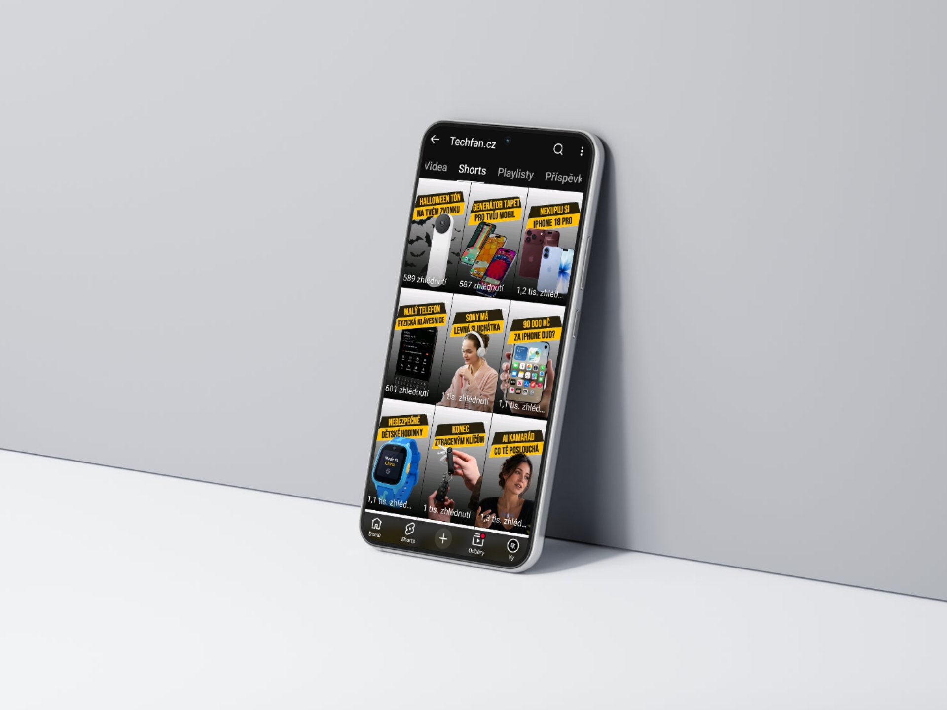 Sklopený smartphone zobrazuje YouTube rozhraní s videi a titulky na šedém pozadí.