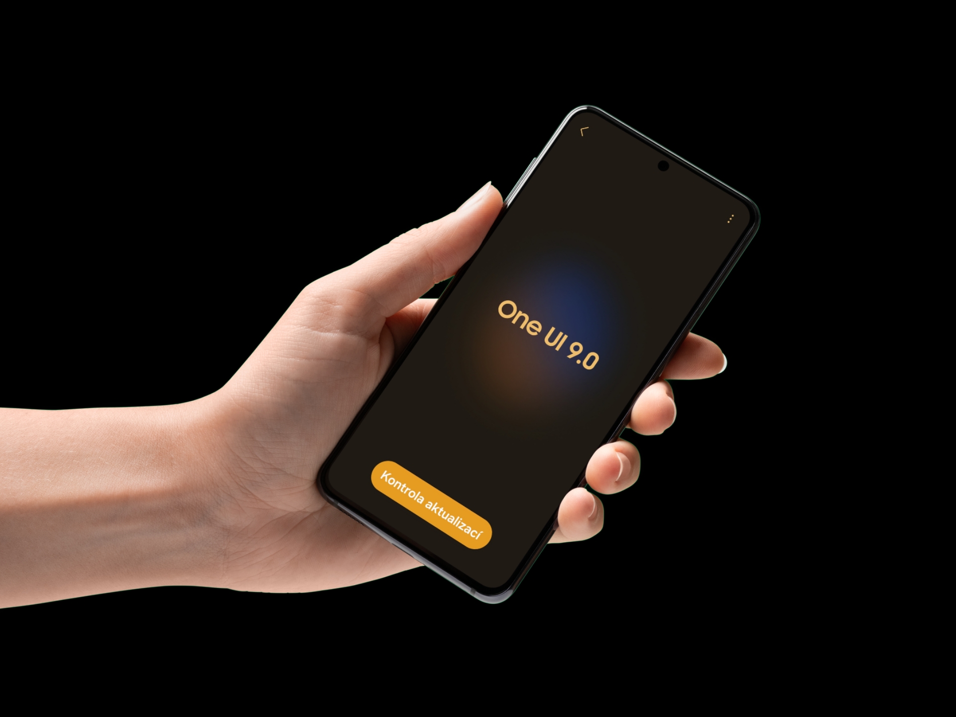 Ruka drží smartphone Samsung s obrazovkou „One UI 9.0“ a tlačítkem „Kontrola aktualizací“ na černém pozadí.
