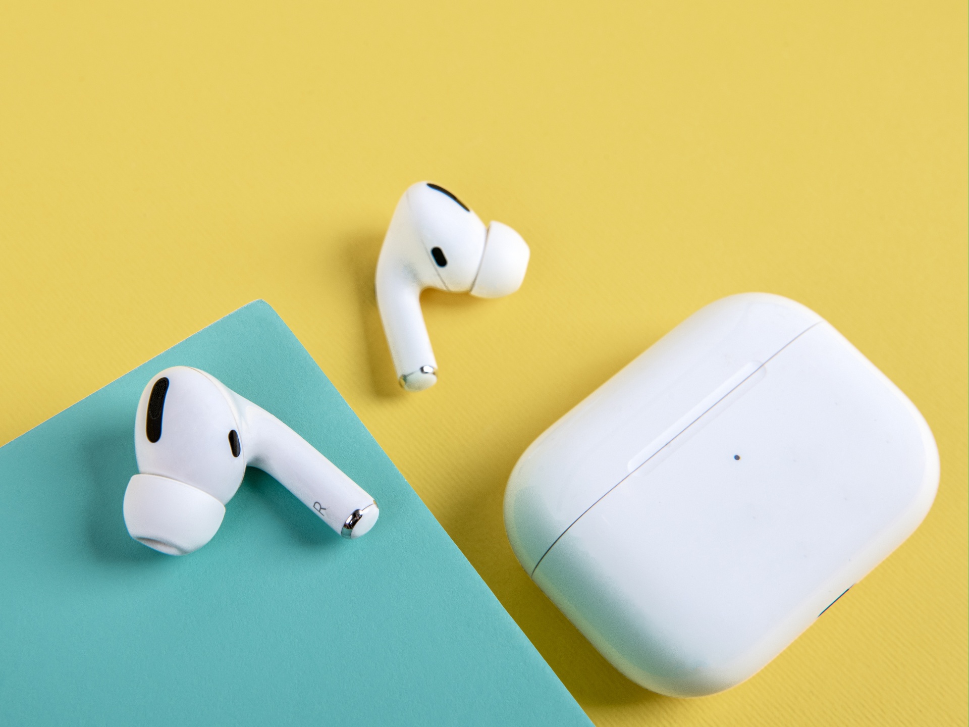Bílé bezdrátové sluchátka Apple Airpods a nabíjecí pouzdro na žlutém a modrém podkladu, detailní záběr.