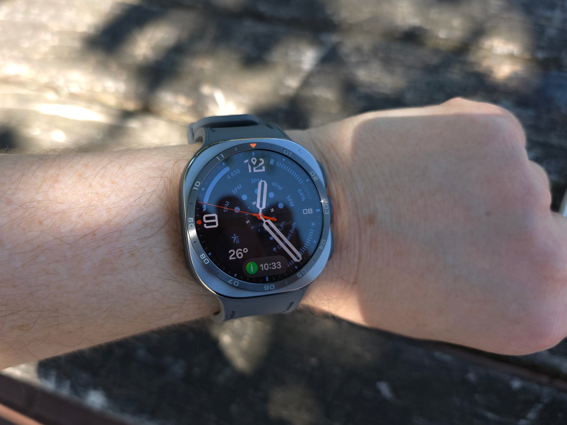 Na zápěstí jsou chytré hodinky Samsung Galaxy Watch Ultra 2 s modrým ciferníkem, ukazují čas a teplotu venku.